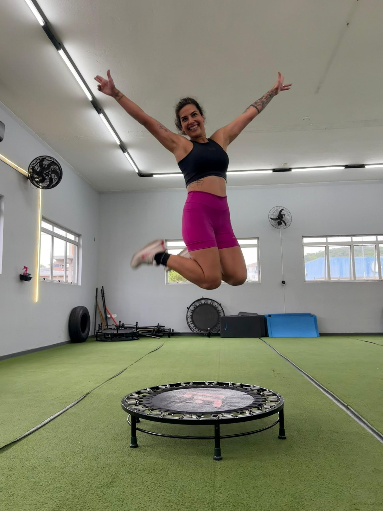 Pri pulando no trampolim, braços erguidos, sorrindo. Energia do Método Pri Jump